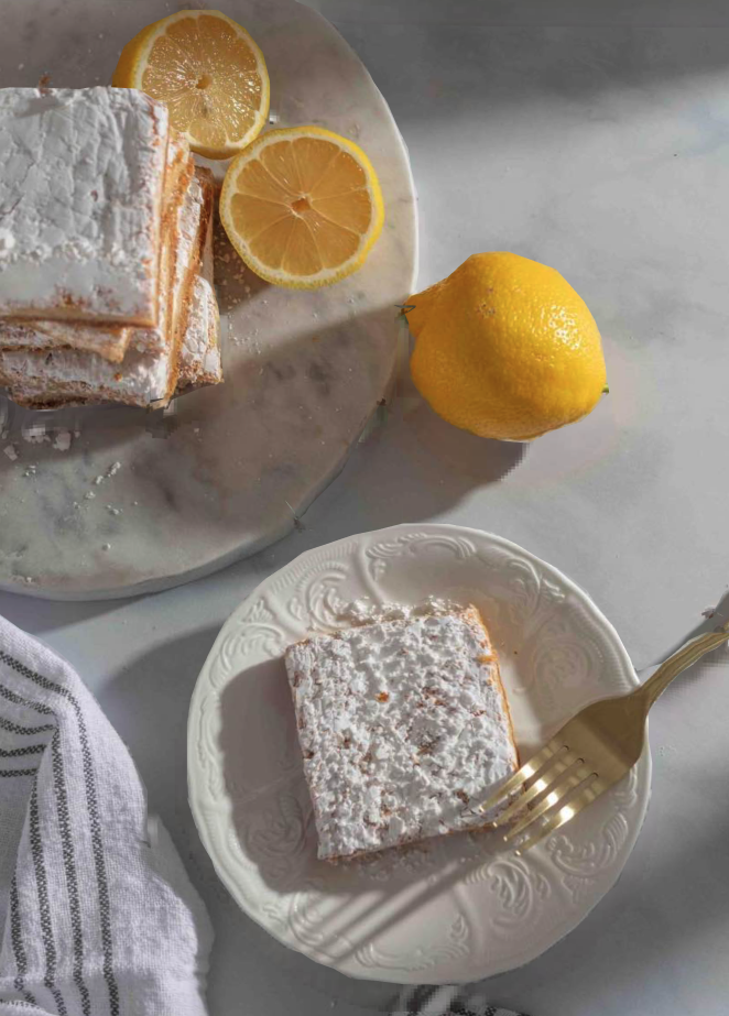 Lemon bars topped with powdered sugar, served on a decorative plate with fresh lemon slices.